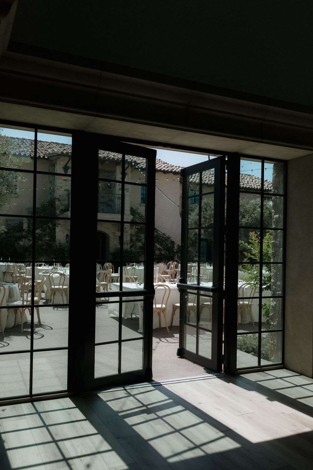 Black-framed French doors with glass panels open to a sunny outdoor patio area with dining tables and chairs.