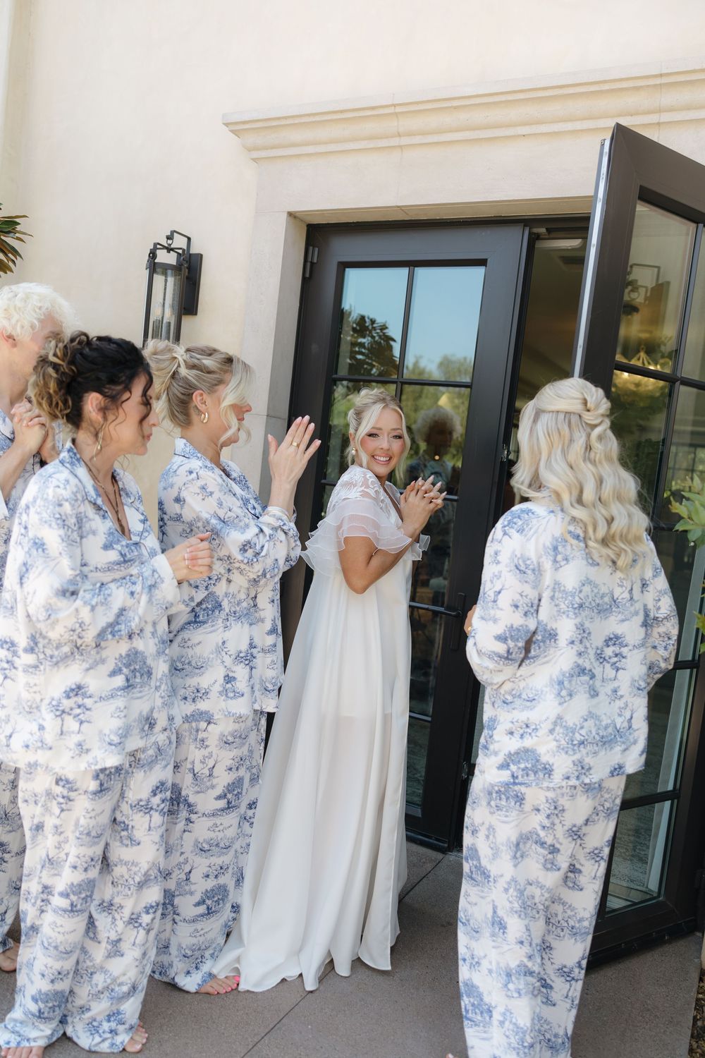 A group wearing matching blue and white floral robes gathers at an entrance door for a special occasion.