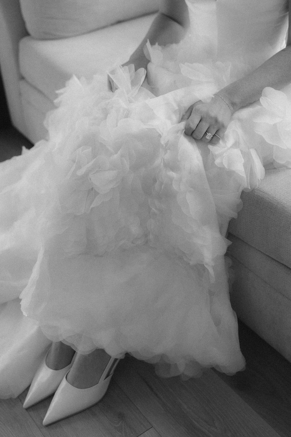 Close-up view of a flowing white tulle wedding dress with white pointed heels visible beneath the layers of fabric.