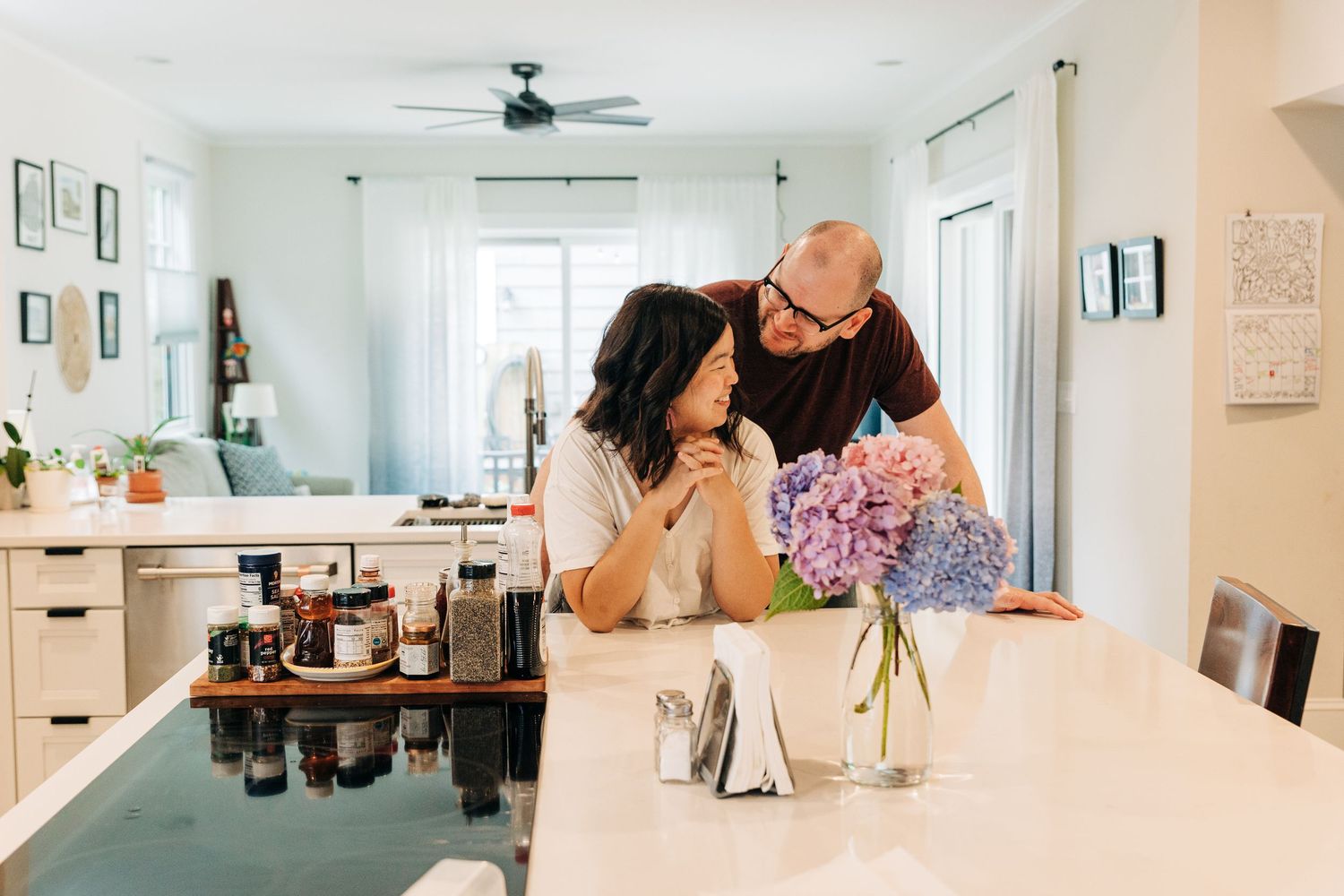 A couple sharing a moment in their bright modern kitchen with a vase of pink flowers on the white counter.
