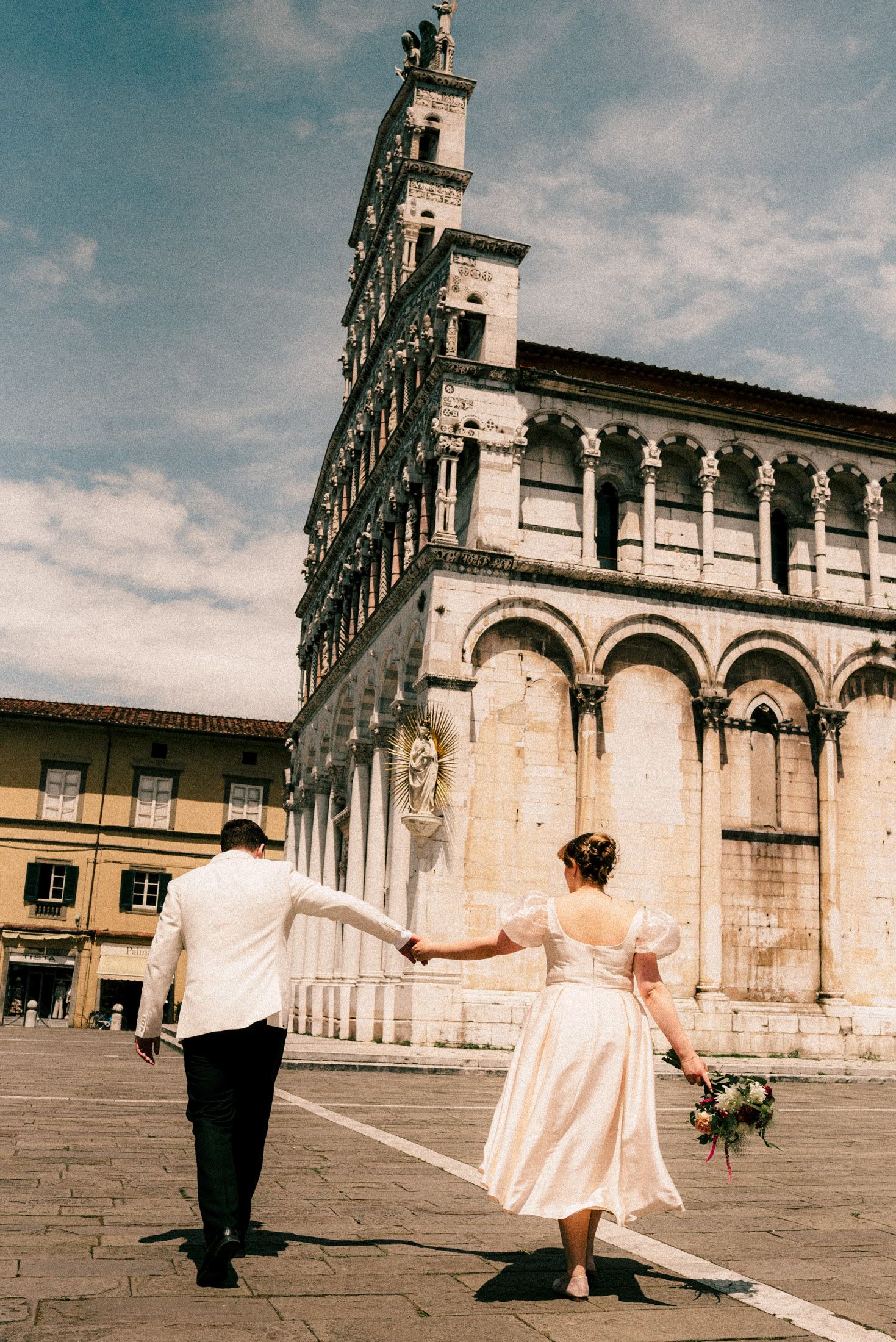 Couple walking hand in hand towards historic Italian church architecture.