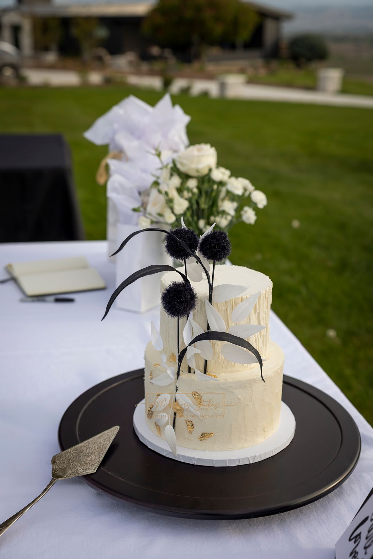Cakes by Blythe, creamy white cake with black and white florals and gold details on table with giflts