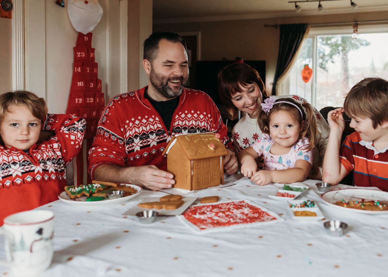 A group of people wearing festive red and white holiday sweaters sit together around a dining table decorated for Christmas.