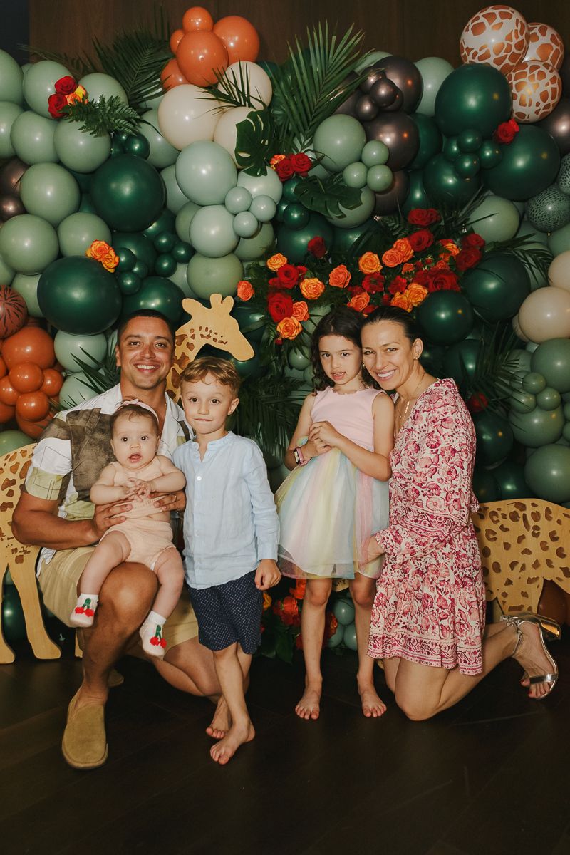 Heartwarming family moment—parents and children gather in front of a lush safari-inspired balloon installation at a high-end baby shower.