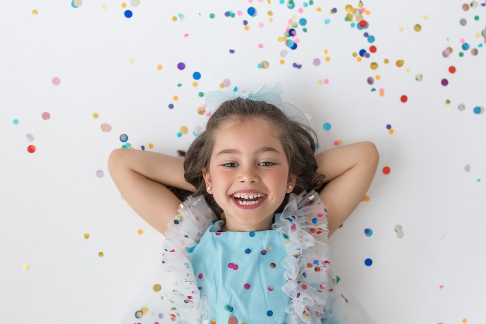 Girl laughing joyfully while twirling in her birthday outfit on a white seamless backdrop.