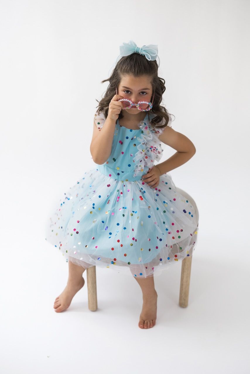 Girl laughing joyfully while twirling in her birthday outfit on a white seamless backdrop.