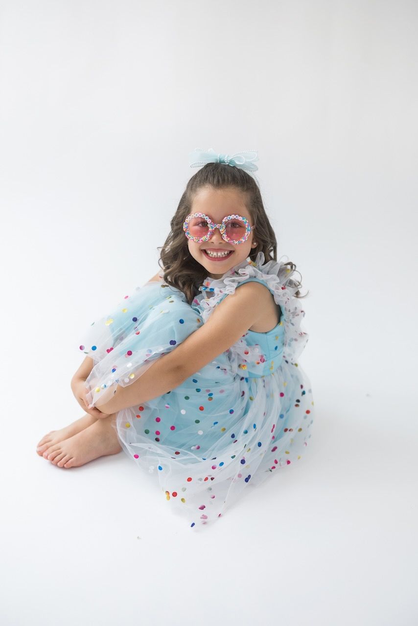 Girl laughing joyfully while twirling in her birthday outfit on a white seamless backdrop.