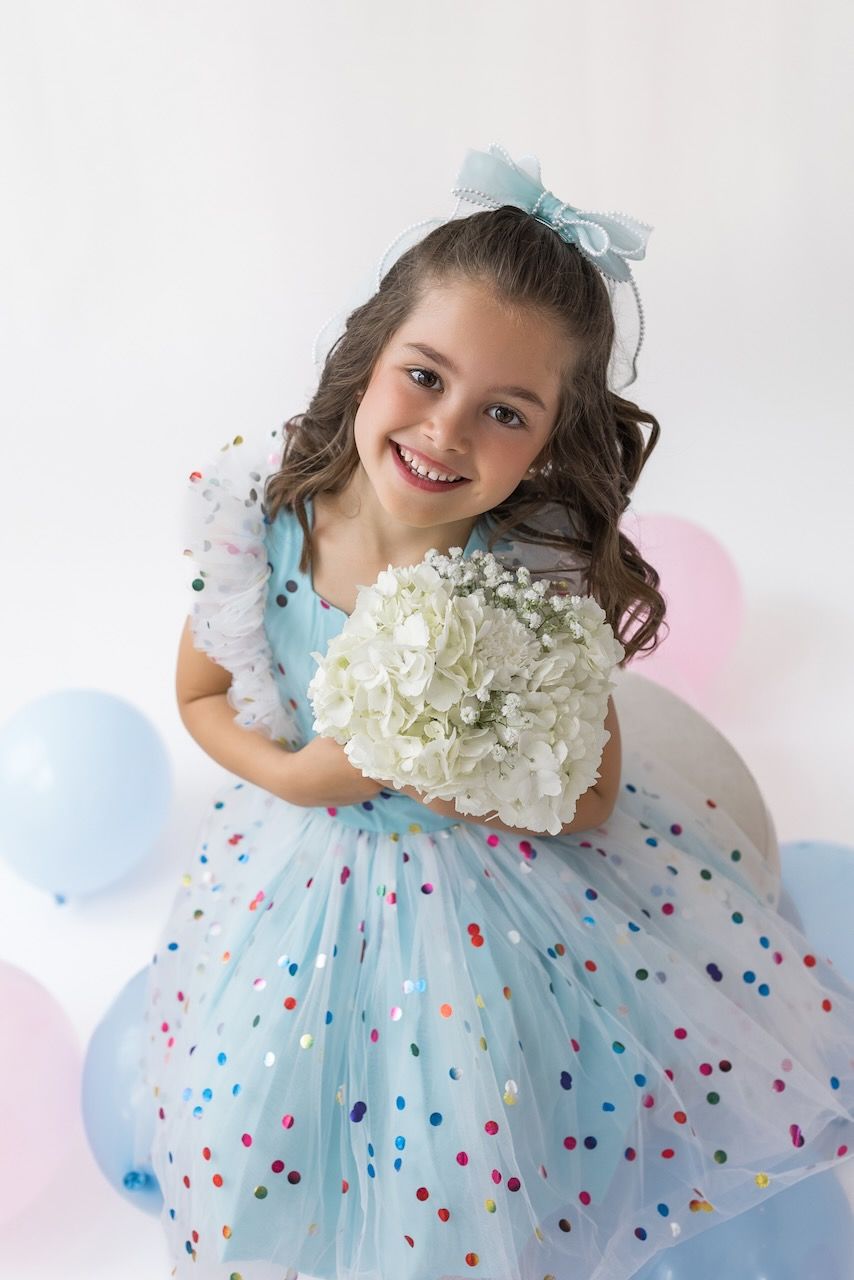 Girl laughing joyfully while twirling in her birthday outfit on a white seamless backdrop.