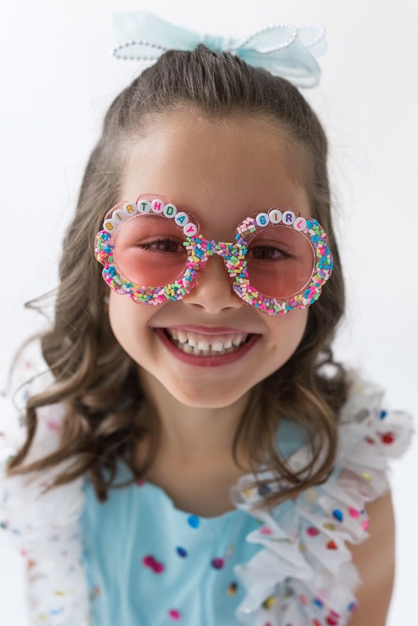 Girl laughing joyfully while twirling in her birthday outfit on a white seamless backdrop.