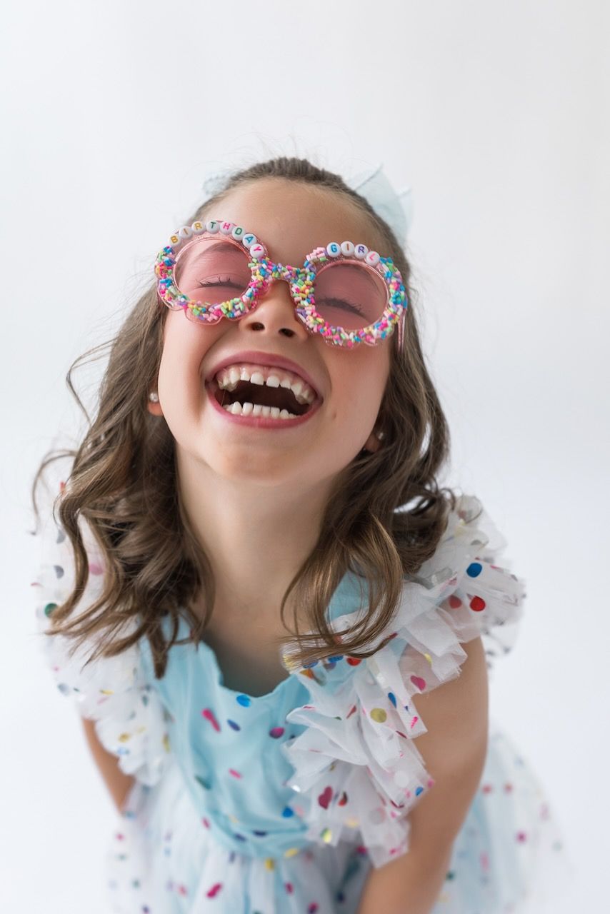 Girl laughing joyfully while twirling in her birthday outfit on a white seamless backdrop.