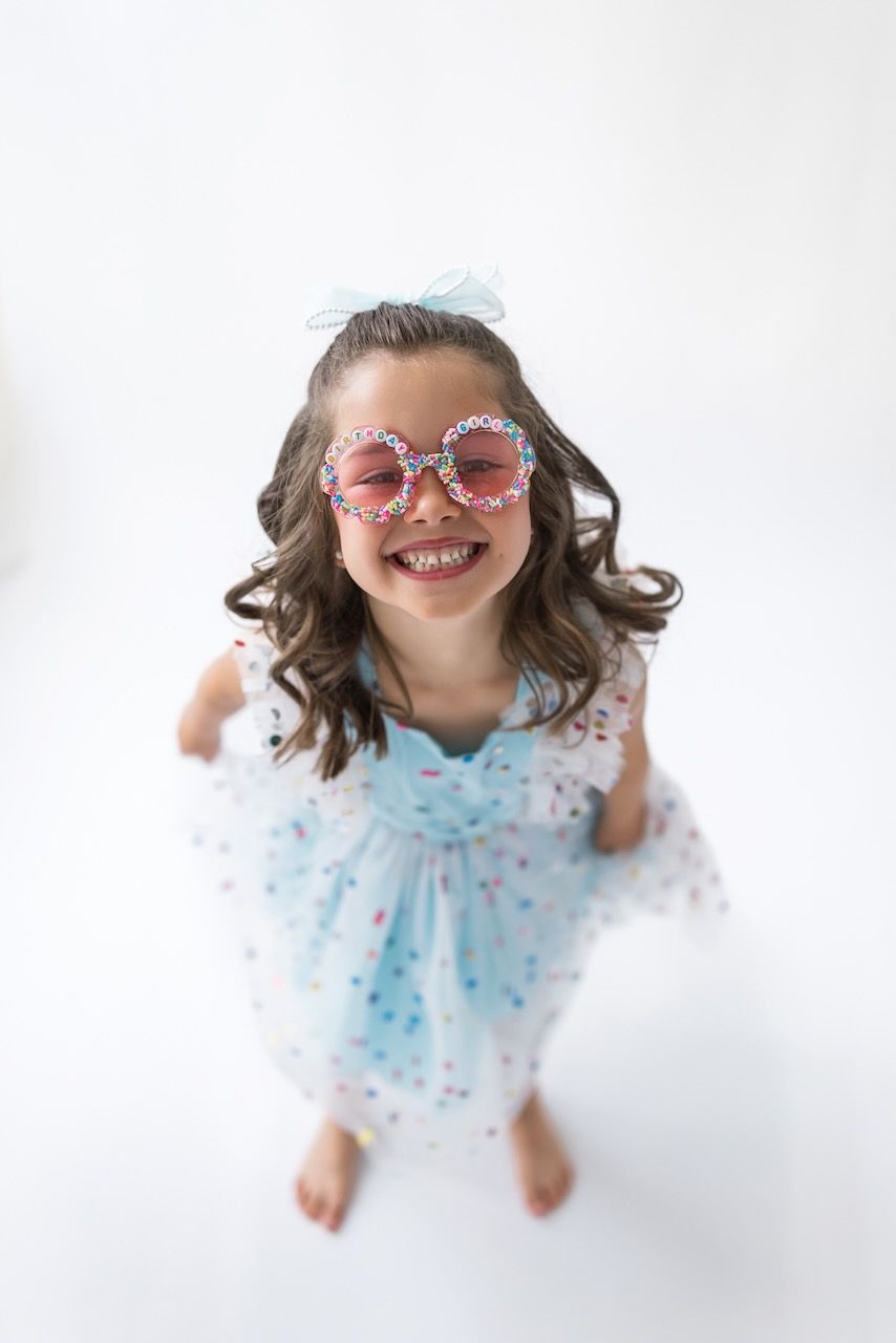 Girl laughing joyfully while twirling in her birthday outfit on a white seamless backdrop.