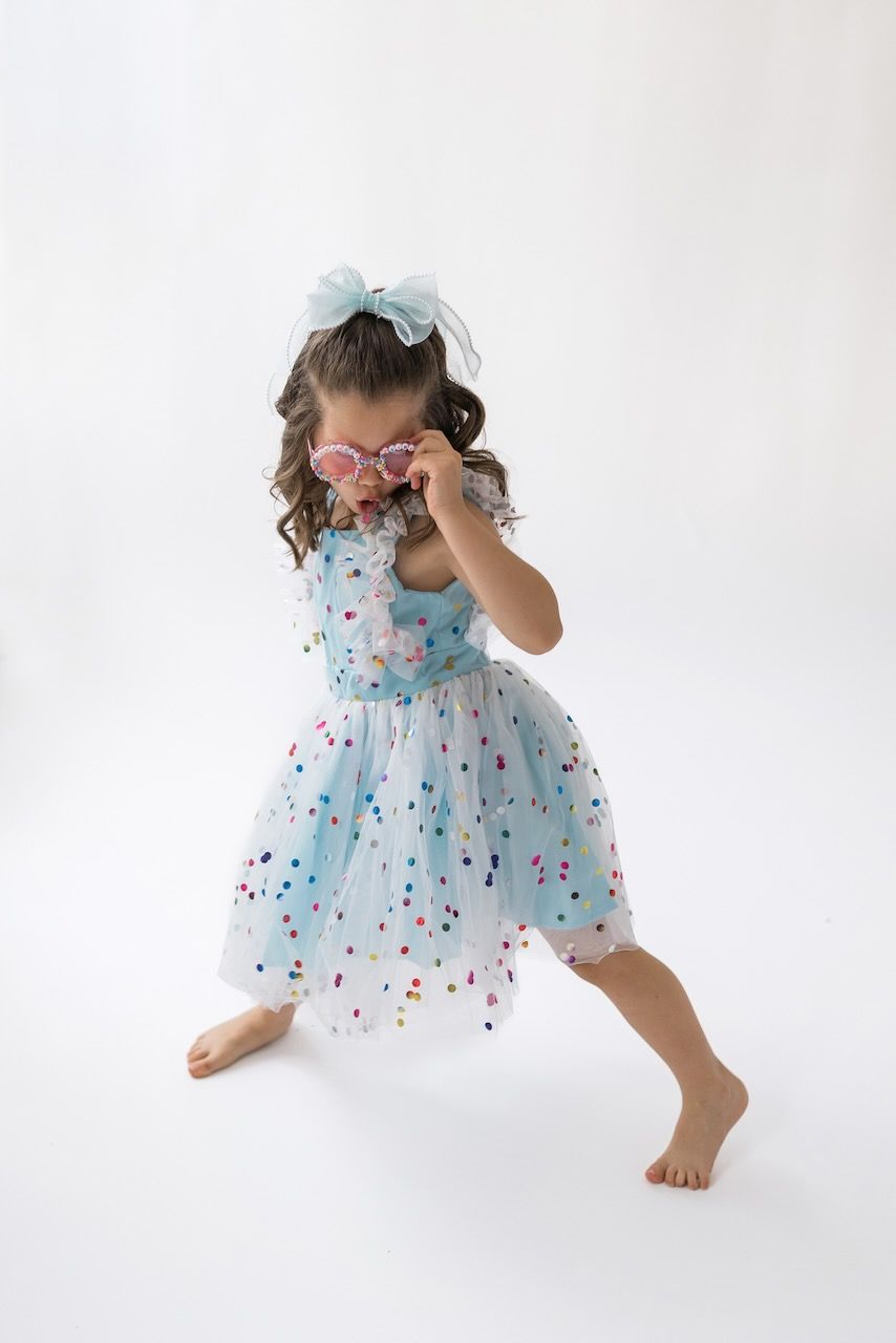 Girl laughing joyfully while twirling in her birthday outfit on a white seamless backdrop.