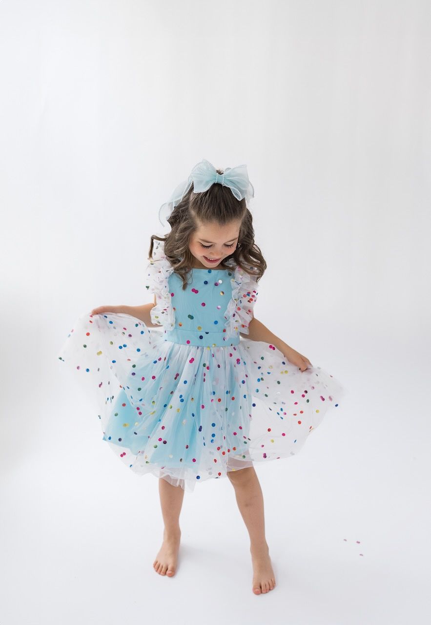 Girl laughing joyfully while twirling in her birthday outfit on a white seamless backdrop.