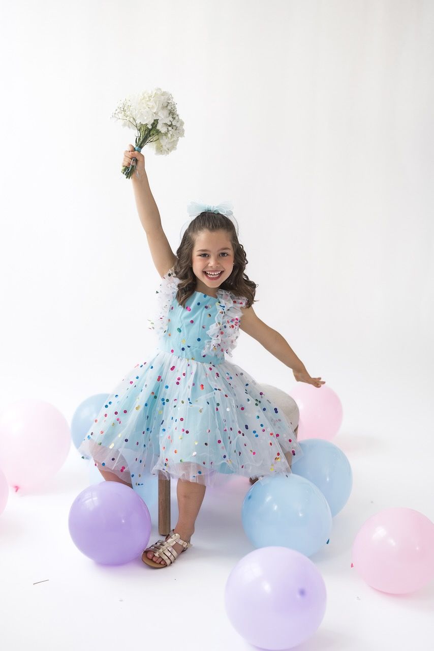 Girl laughing joyfully while twirling in her birthday outfit on a white seamless backdrop.