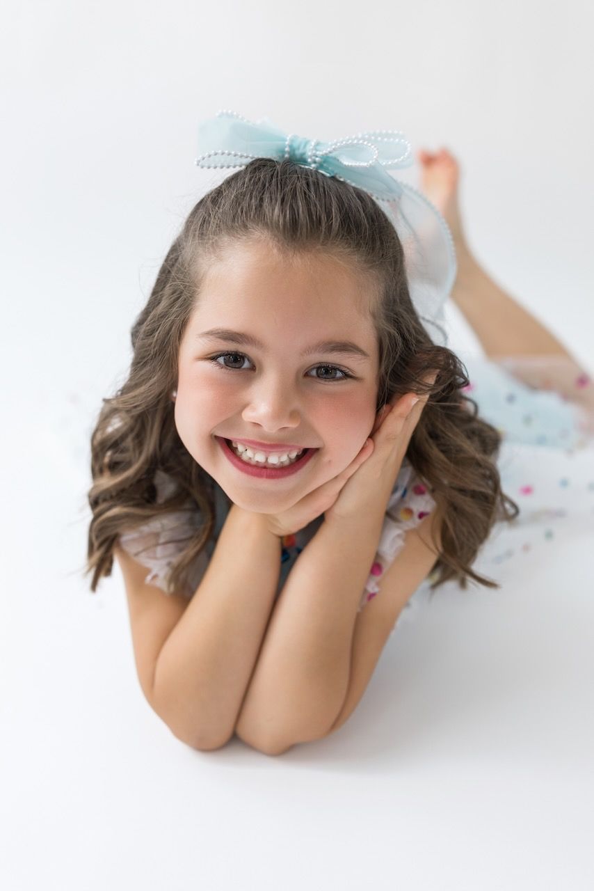 Girl laughing joyfully while twirling in her birthday outfit on a white seamless backdrop.
