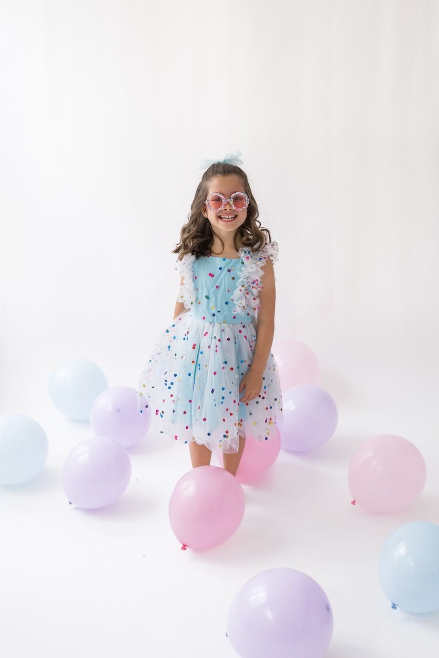 Girl laughing joyfully while twirling in her birthday outfit on a white seamless backdrop.
