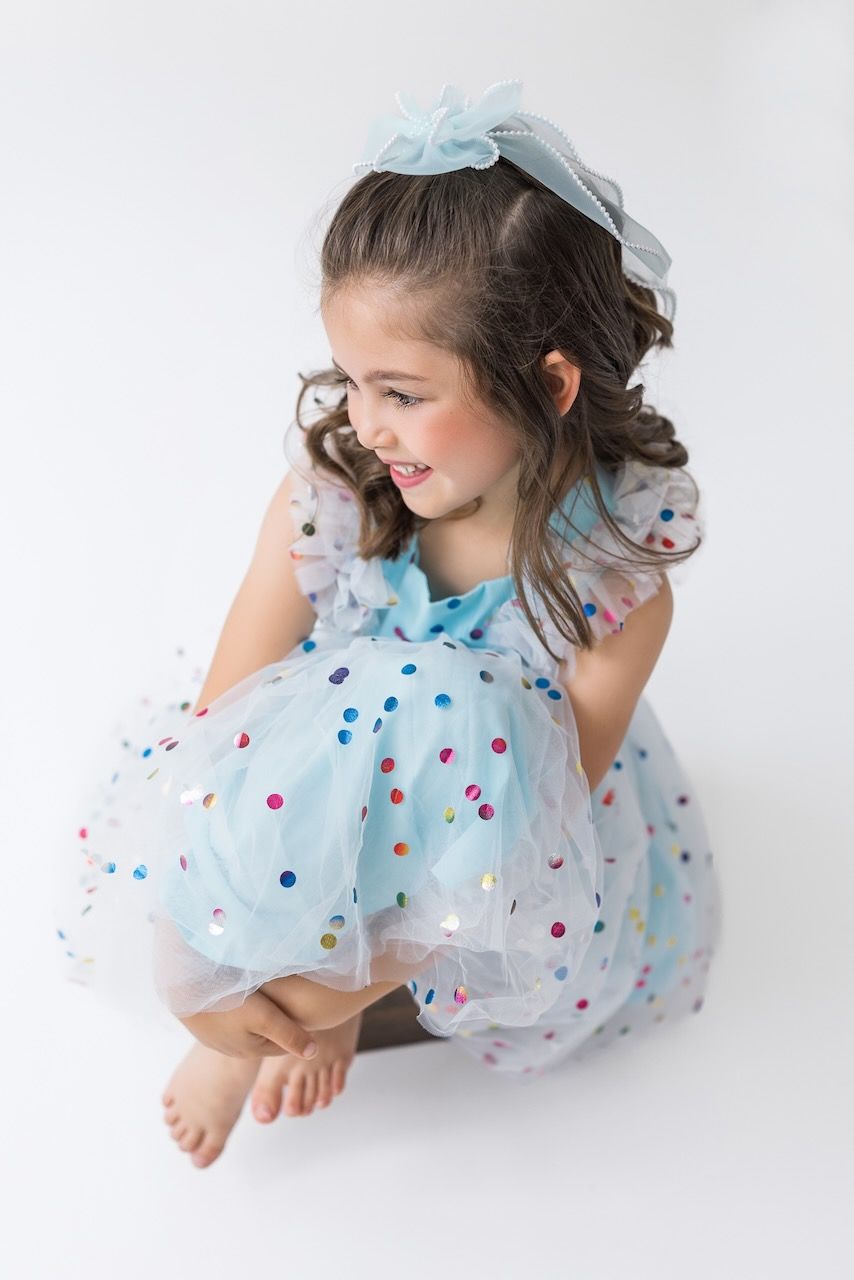 Girl laughing joyfully while twirling in her birthday outfit on a white seamless backdrop.