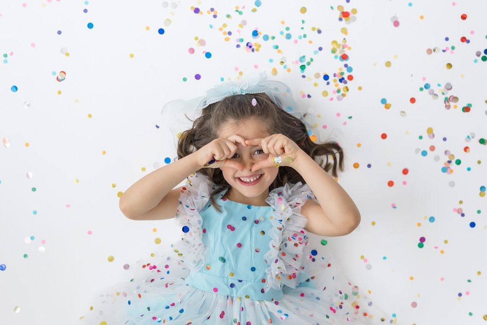 Girl laughing joyfully while twirling in her birthday outfit on a white seamless backdrop.