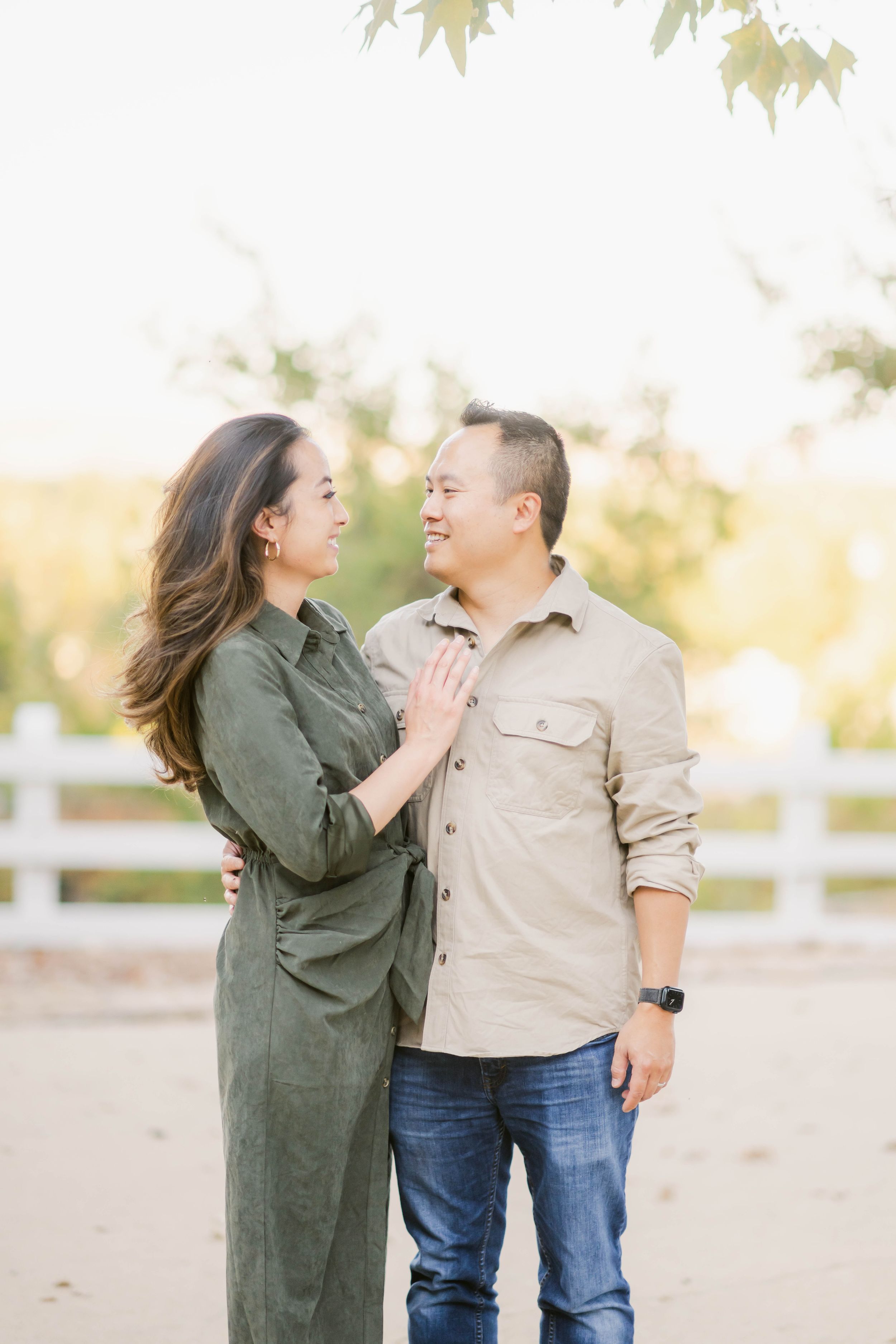 Romantic outdoor couple photoshoot with tan and olive clothing against white fencing and dreamy golden sunlight.