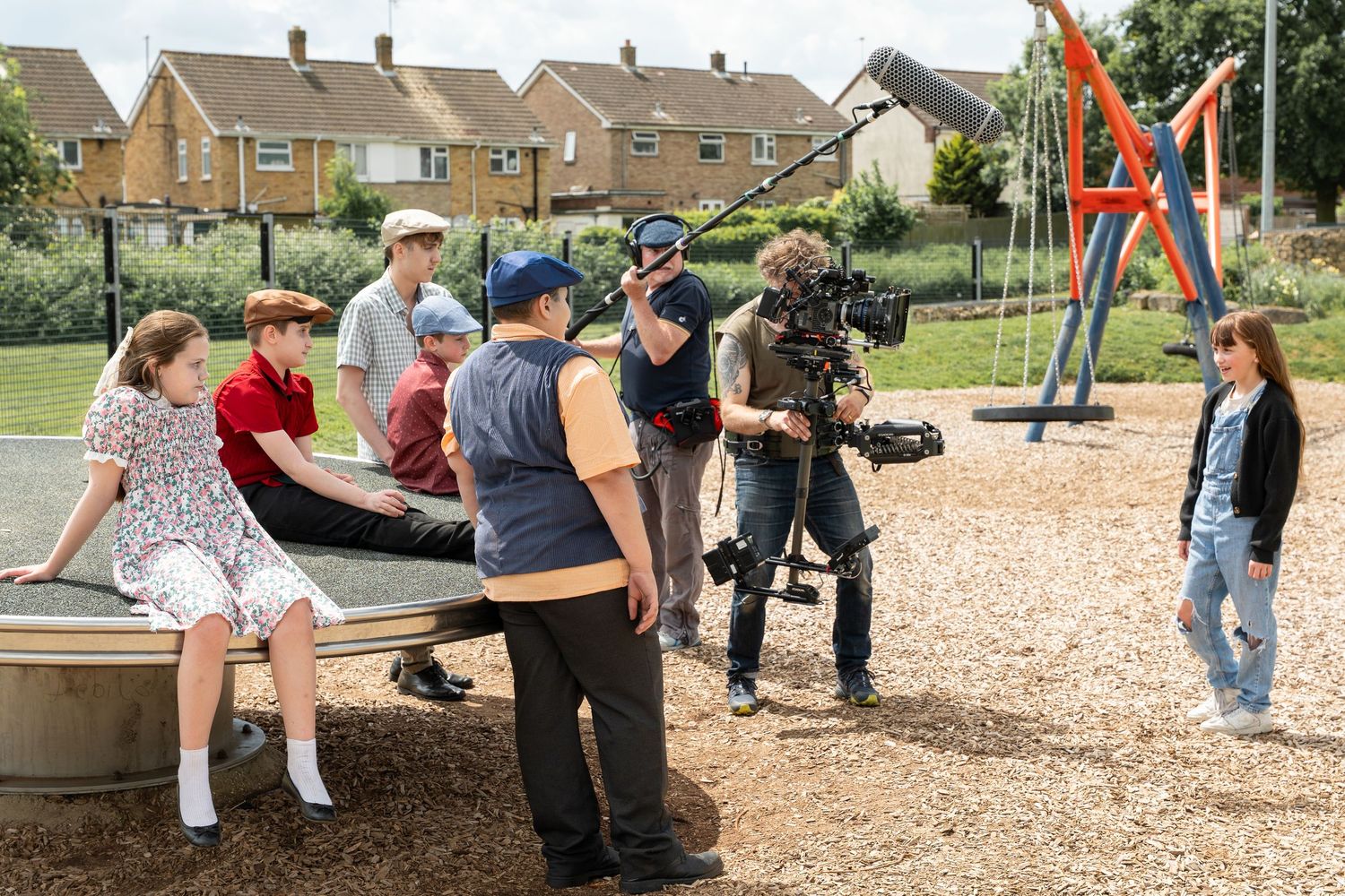 Behind the scenes film crew shooting on location at a playground with camera equipment and cast members.