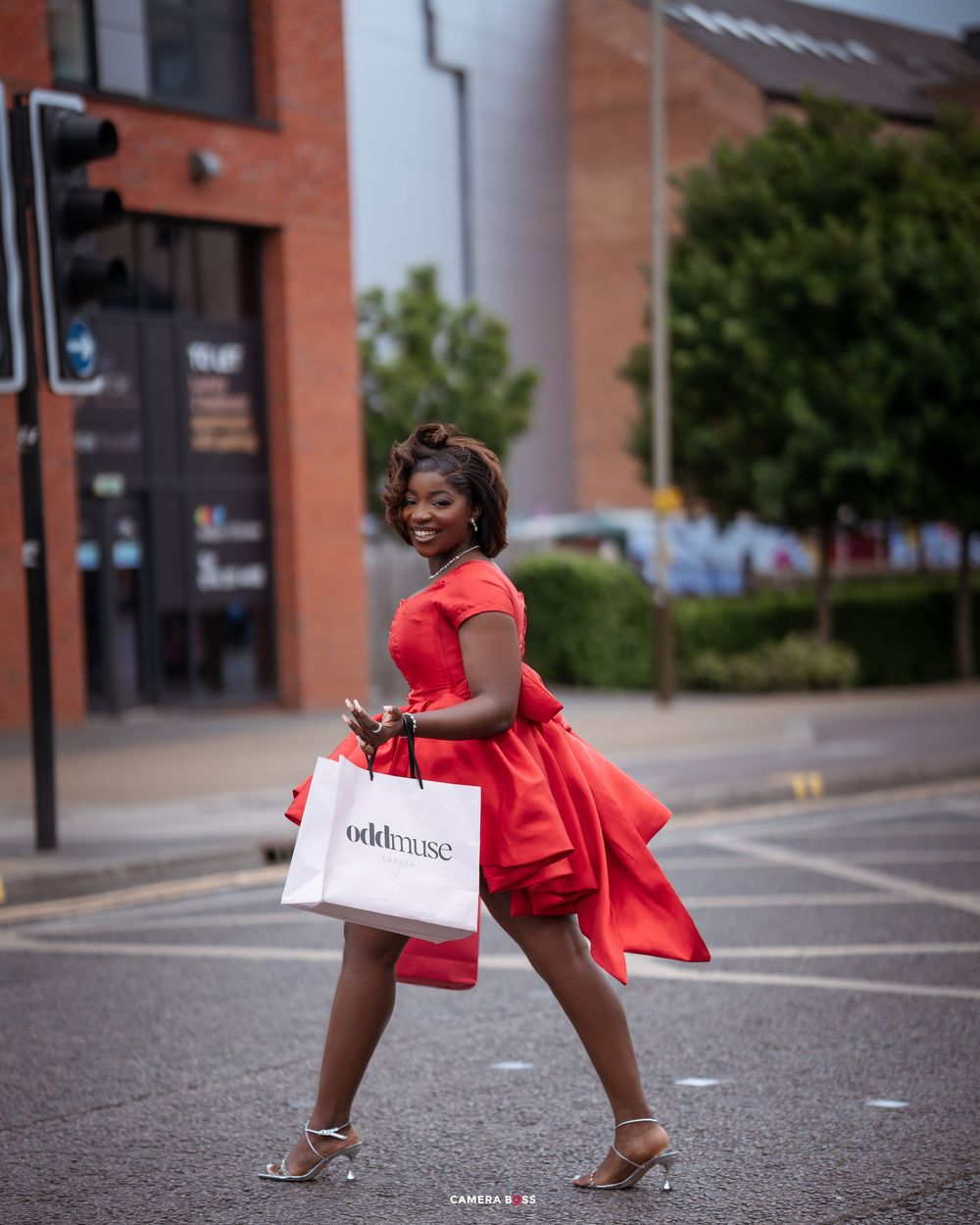 Person in red dress and heels poses playfully in an empty parking lot while holding shopping bags.
