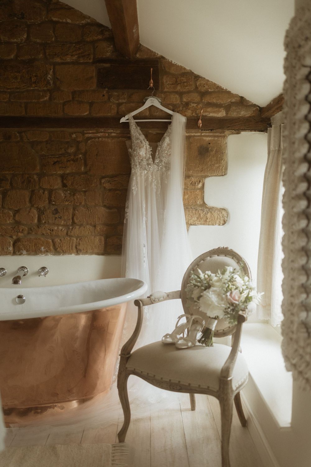 Vintage clawfoot bathtub sits against exposed brick wall with white curtains in rustic bathroom interior.