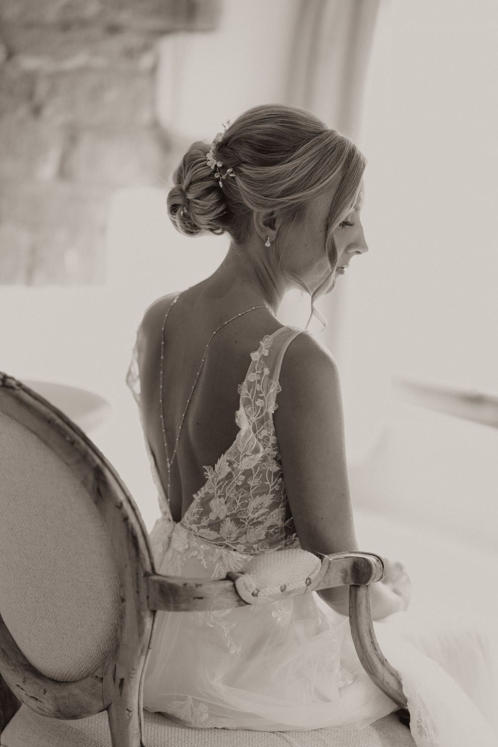 A bride in a lace wedding dress with an open back design sits elegantly at Crockwell Farm wedding