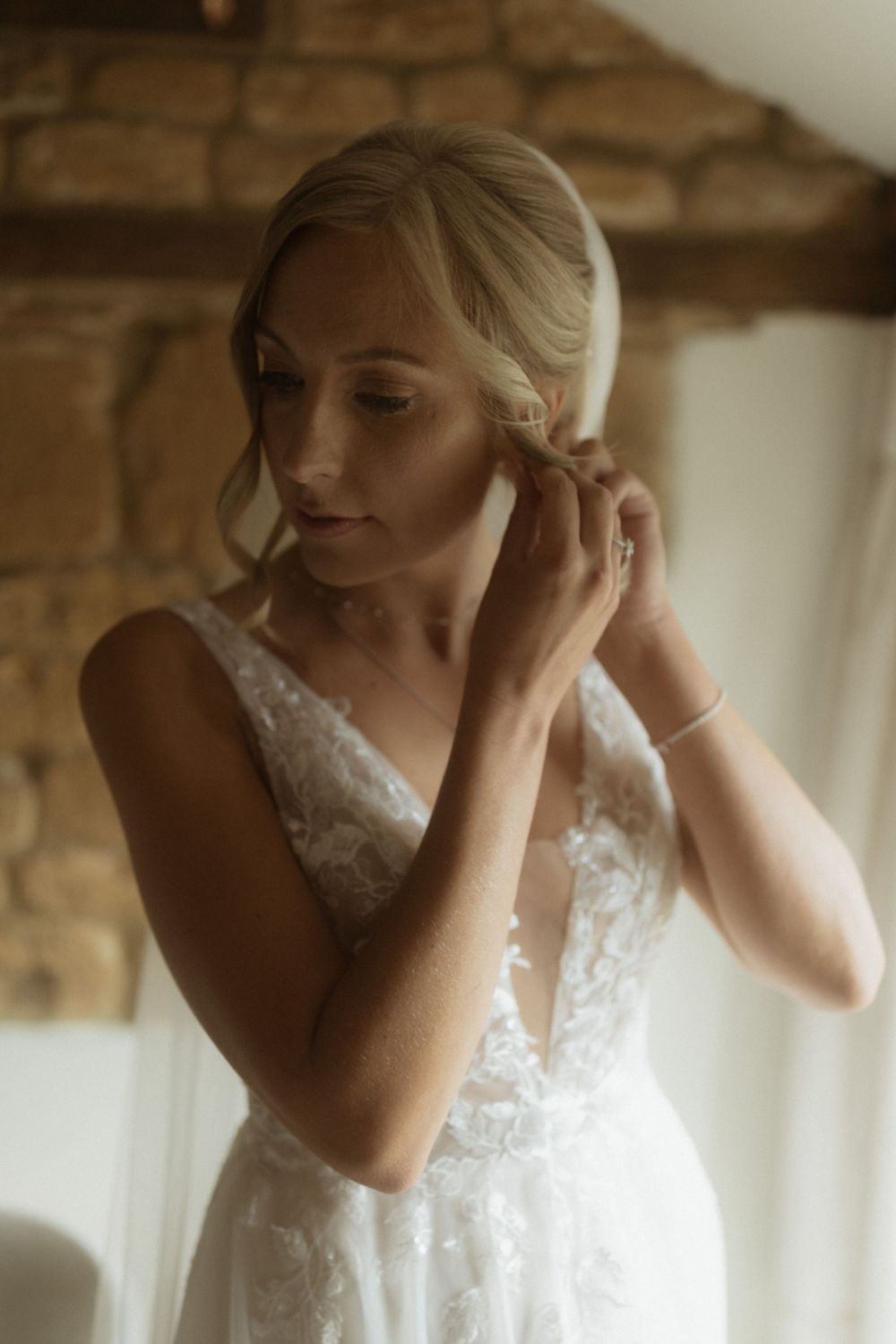 A bride wearing a lace white dress touches her hair while getting ready at Crockwell Farm wedding