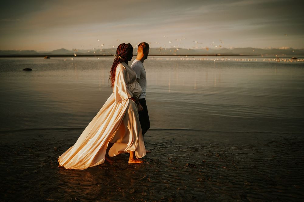 Maternity portrait photography of couple walking along kye bay beach by ocean during golden hour Comox Valley Vancouver Island photographer