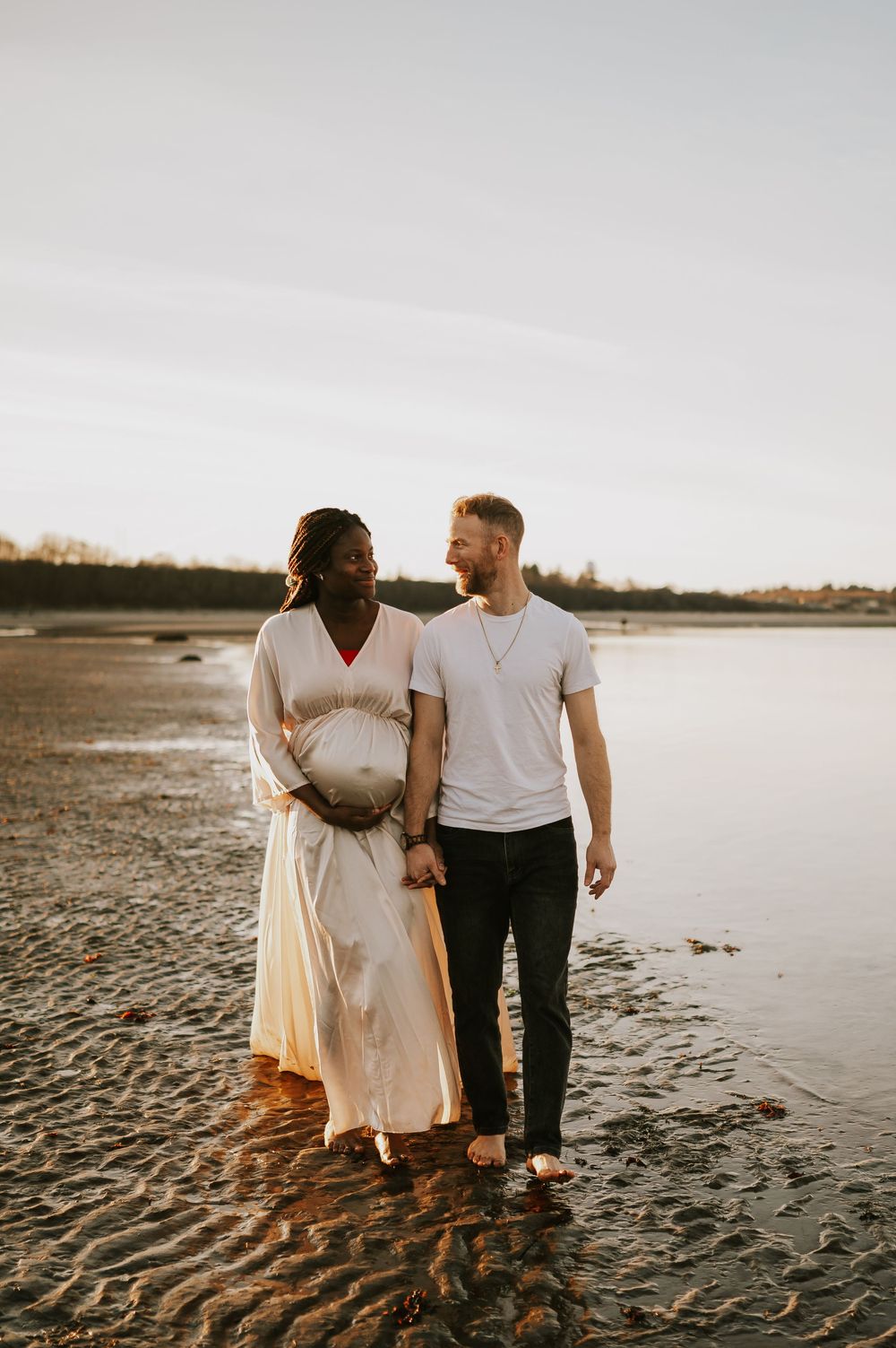 Maternity portrait photography of couple walking along kye bay beach by ocean during golden hour Comox Valley Vancouver Island photographer