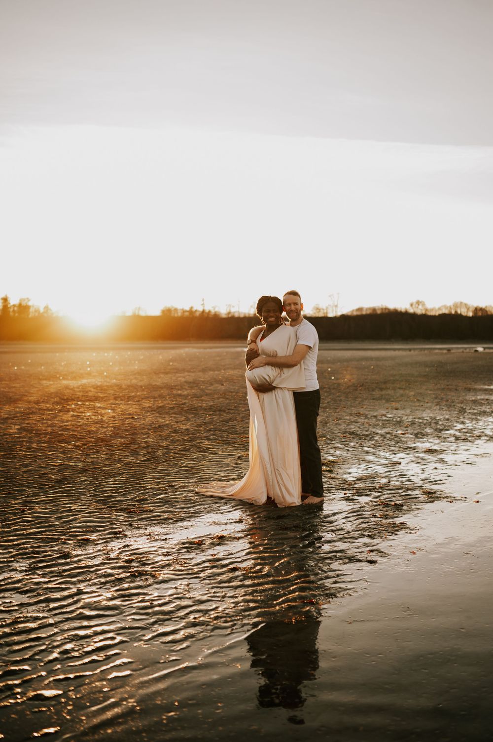 Maternity photography of couple holding bump at kye bay beach by ocean with sunset glowing Comox Valley Vancouver Island photographer