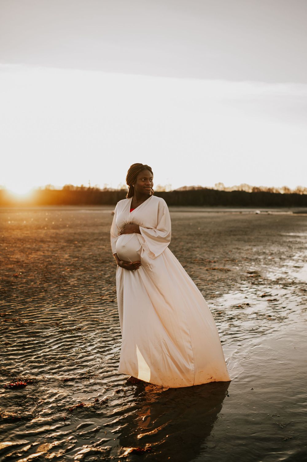 Maternity photography of woman holding bump at kye bay beach by ocean with sunset glowing Comox Valley Vancouver Island photographer