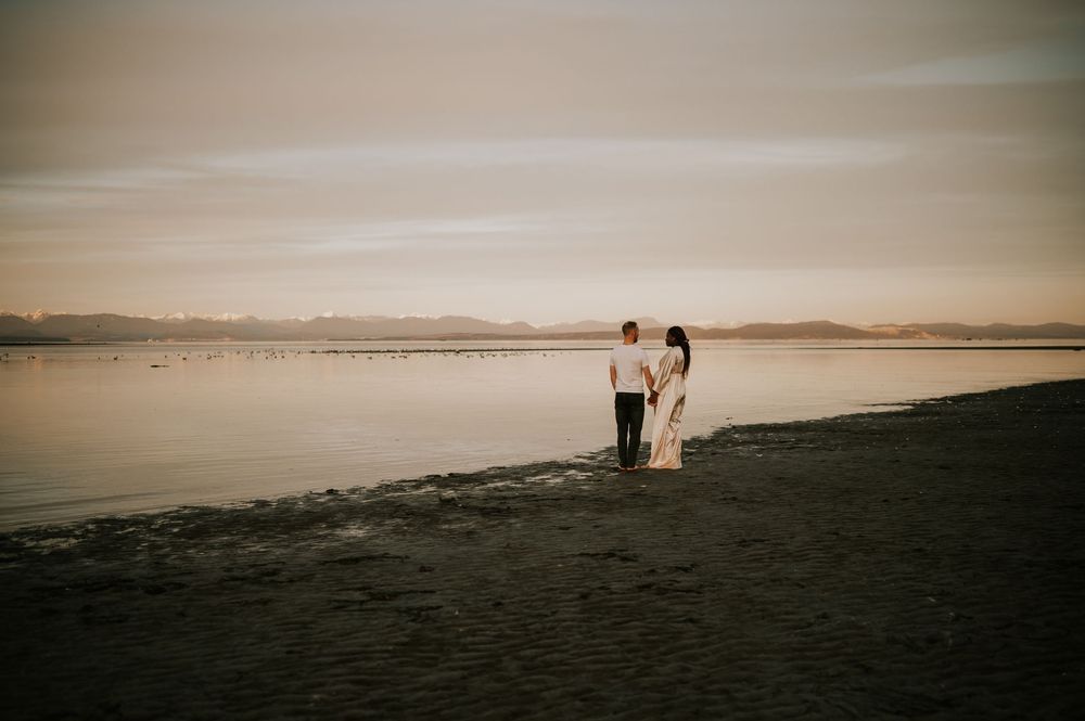 Maternity photography of couple holding bump at kye bay beach by ocean in front of mountains Comox Valley Vancouver Island photographer