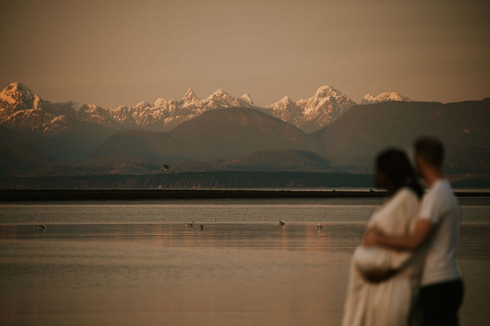 Maternity photoshoot of couple holding bump at kye bay beach by ocean in front of mountains Comox Valley Vancouver Island photographer
