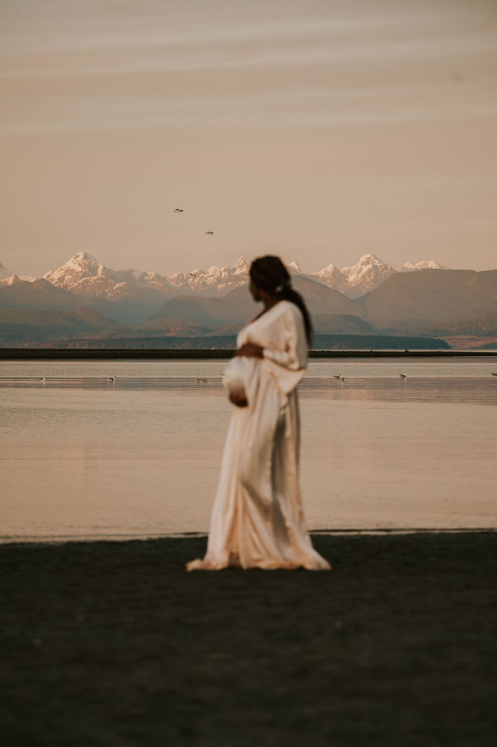 Maternity photography of mother holding bump at kye bay beach by ocean in front of mountains Comox Valley Vancouver Island photographer