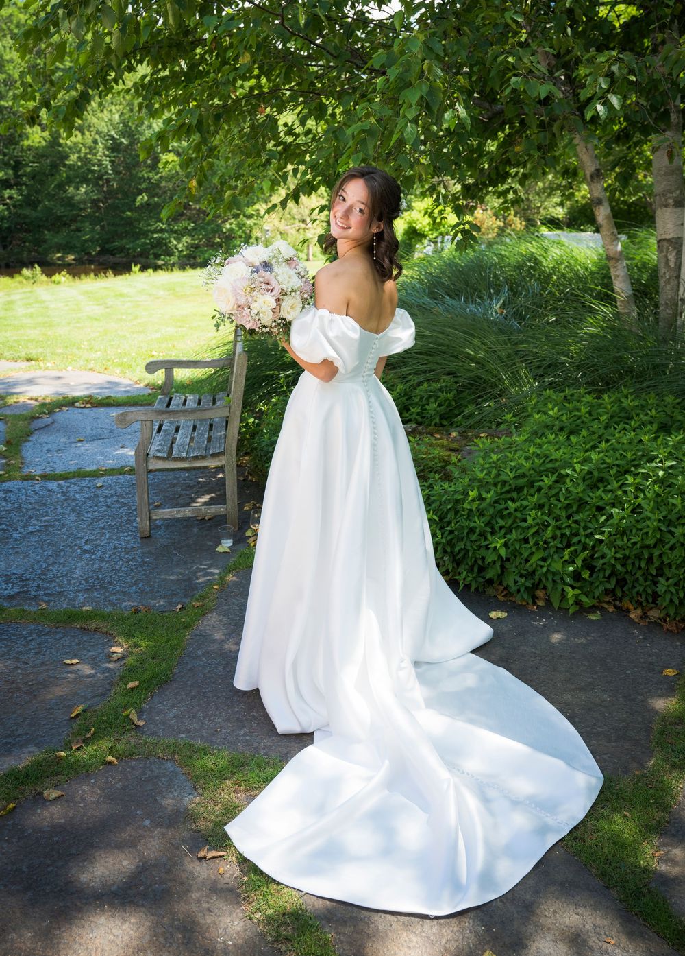 A stunning white wedding gown with off-shoulder design and long train photographed in a garden setting.