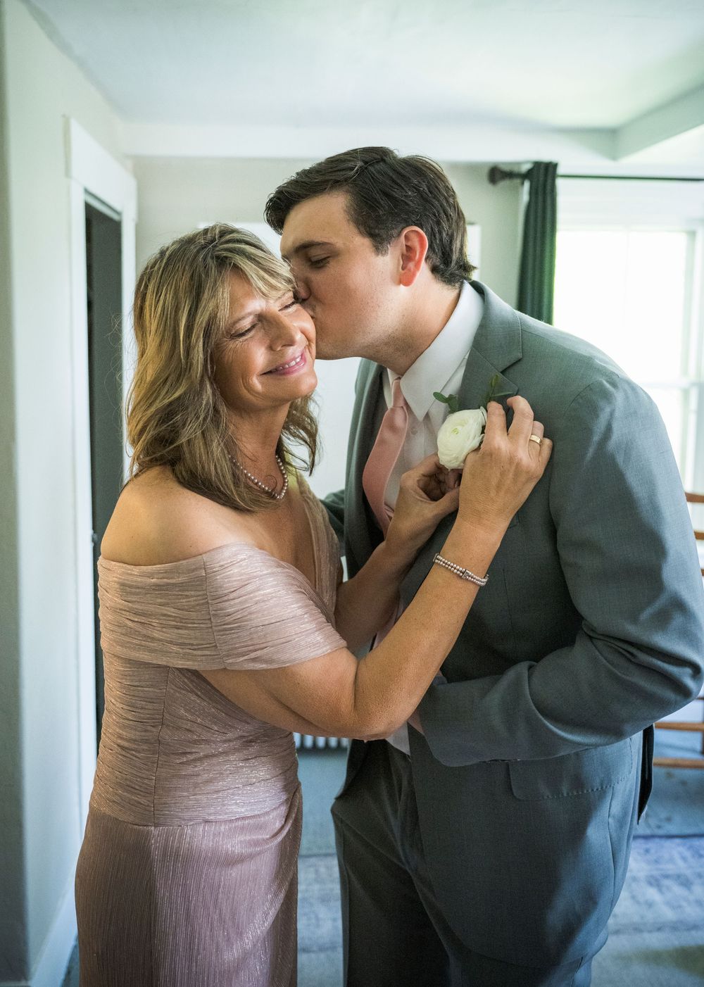 A tender moment shared between a mother and groom in formal attire at a wedding celebration.