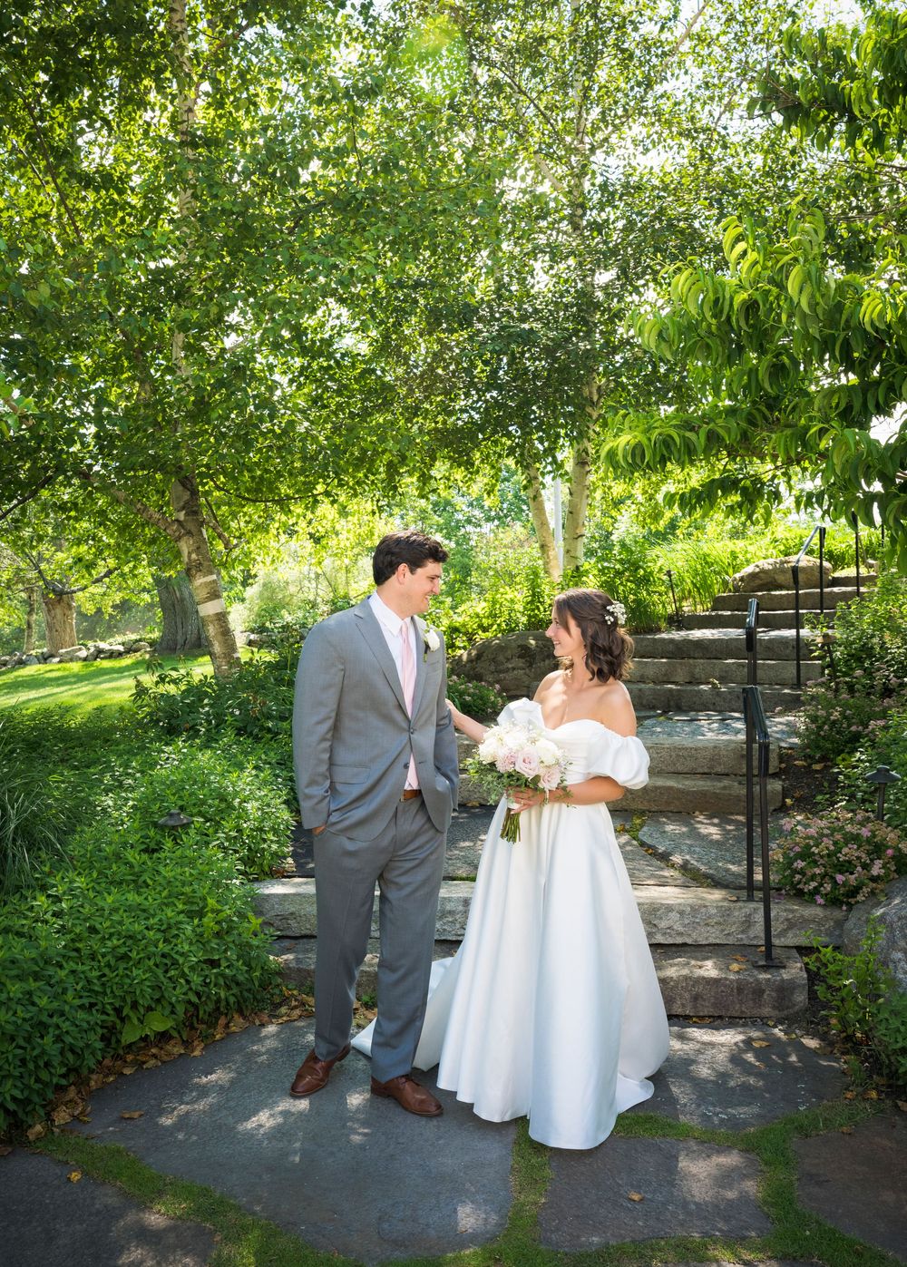 A couple shares a romantic moment on garden steps surrounded by lush green trees and landscaping.