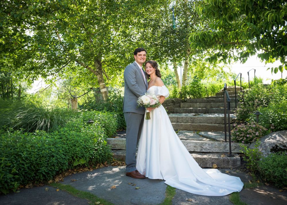 A wedding couple poses together on stone steps surrounded by lush garden greenery.