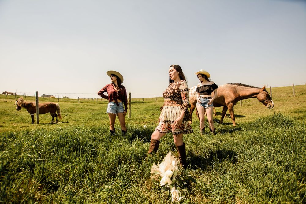 People enjoying an outdoor gathering in a grassy field with horses and farm animals grazing in the background.