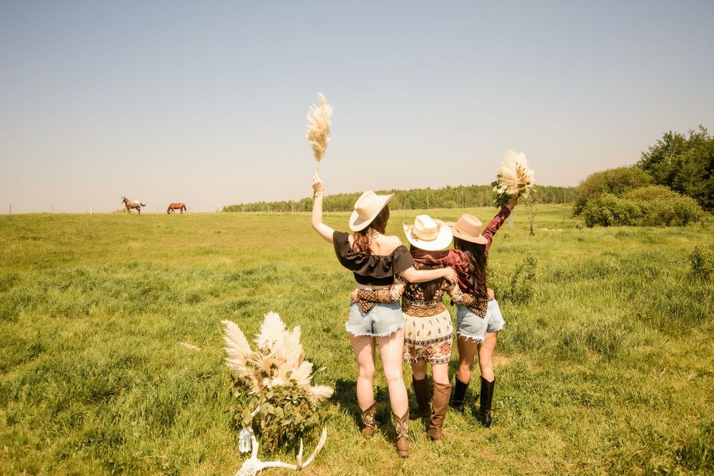 Friends sitting in a grassy meadow with pampas grass decorations and horses in the background.