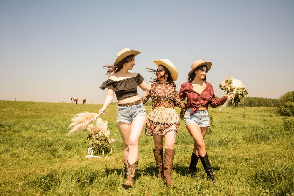 Three friends in cowboy hats and boots dancing together in a sunny field.