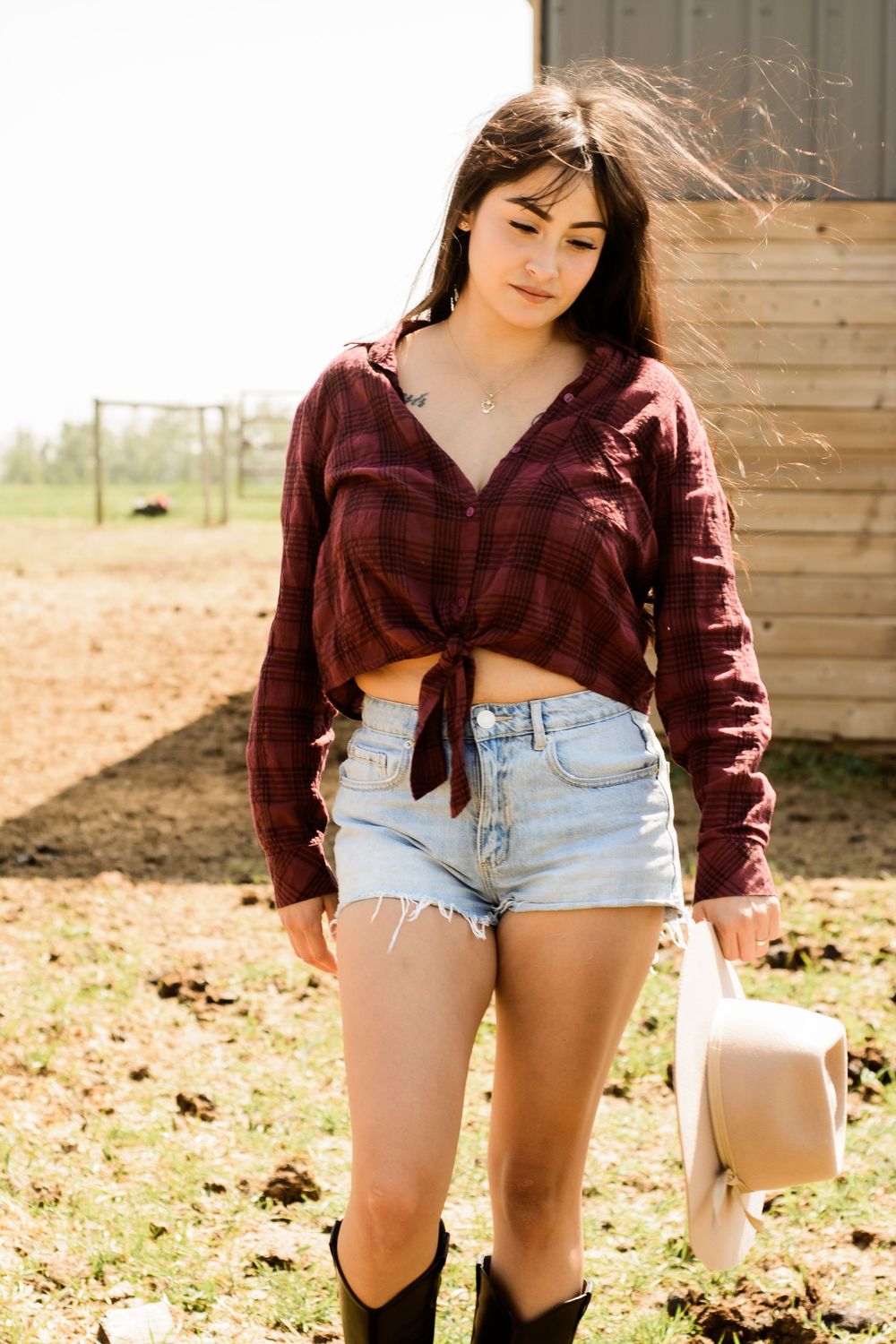 A casual western outfit with denim shorts and burgundy top in a barn setting.