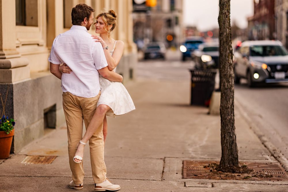 A couple in casual attire embracing on a city sidewalk on a sunny afternoon.