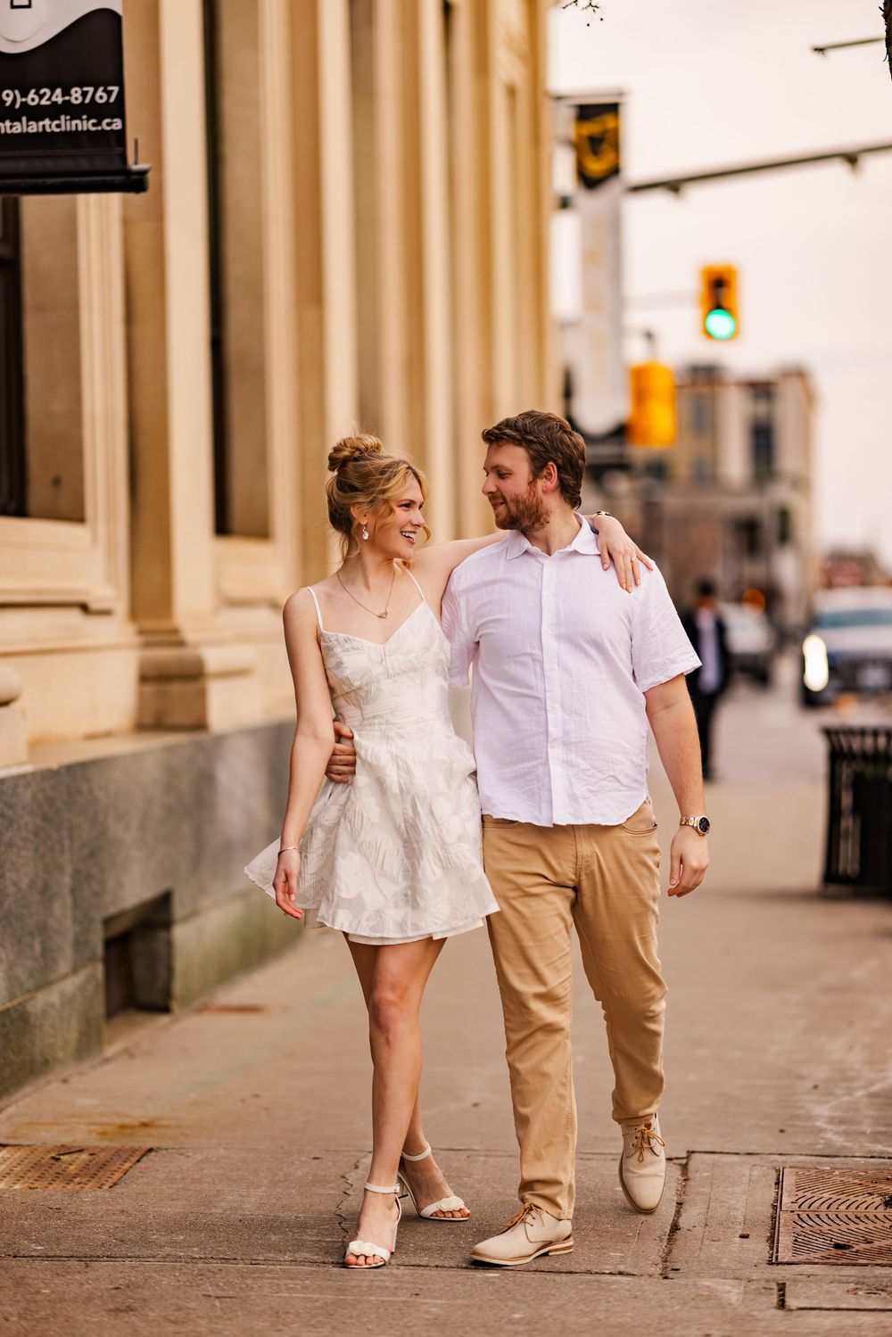 A couple walking together on a city sidewalk, wearing casual attire on a sunny afternoon.