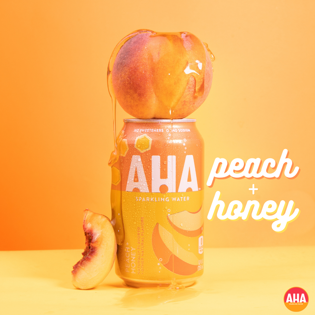 A can of AHA Peach and Honey sparkling water with fresh peaches against an orange background.