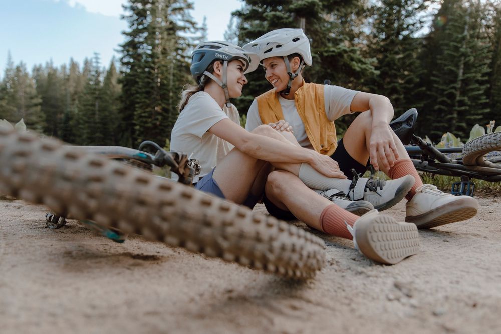 Two mountain bikers in helmets take a break on dirt trail beside their bikes in a forested setting at Lake Tahoe
