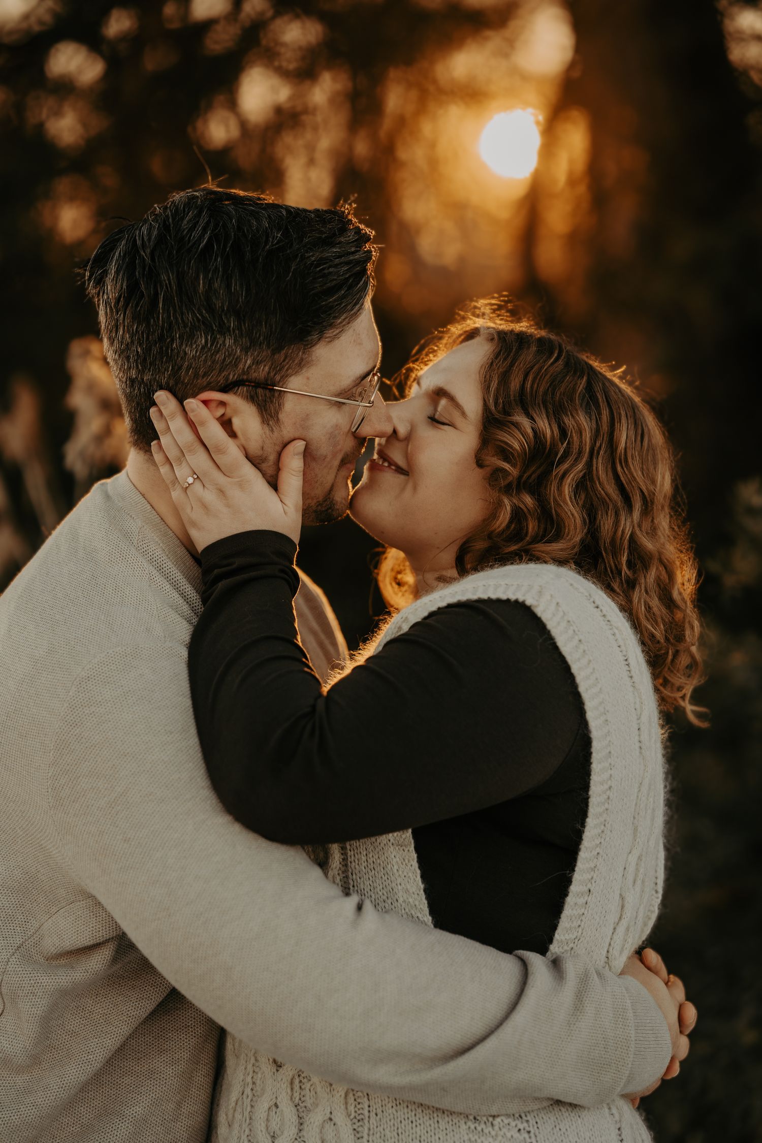 A romantic couple embraces in golden sunset light while sharing an intimate moment among glowing bokeh.