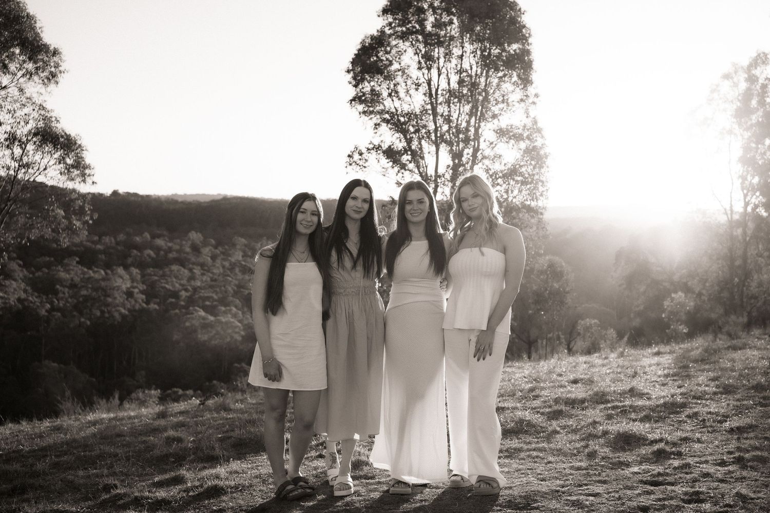 Silhouetted figures in white dresses stand together against a sunlit natural backdrop creating a dreamy atmosphere.