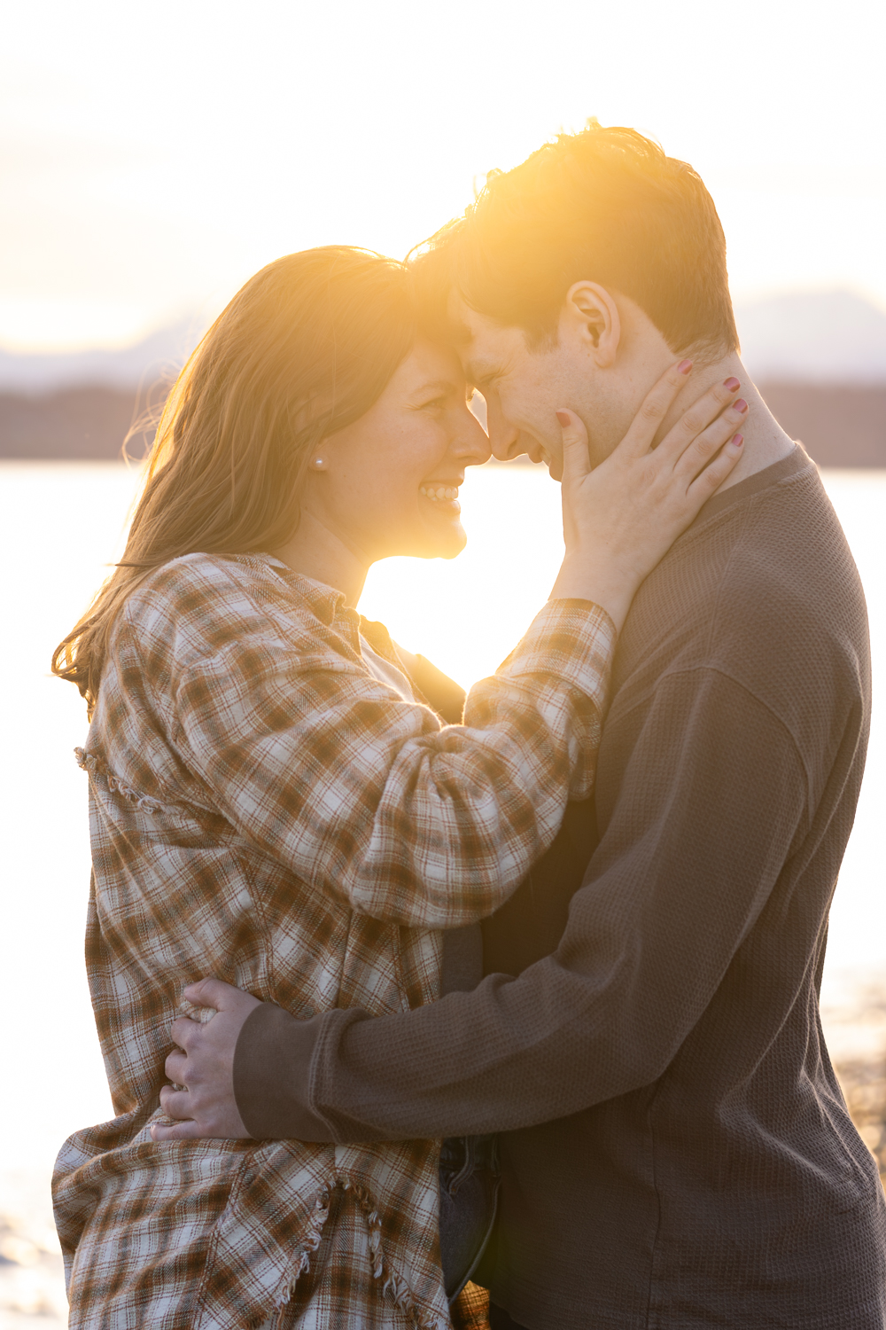 A romantic couple shares an intimate moment at sunset by the water while wearing casual clothing.